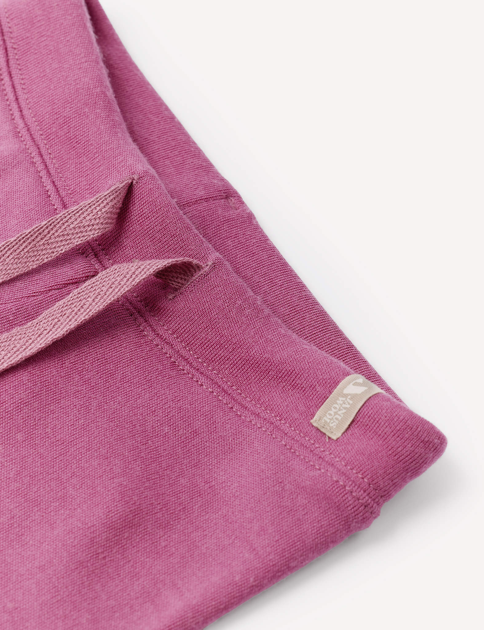 Close-up of the Pants – Merino Baby AirWool in pink, showcasing an adjustable drawcord and a small beige tag with logo and text on the waistband, set against a white background.