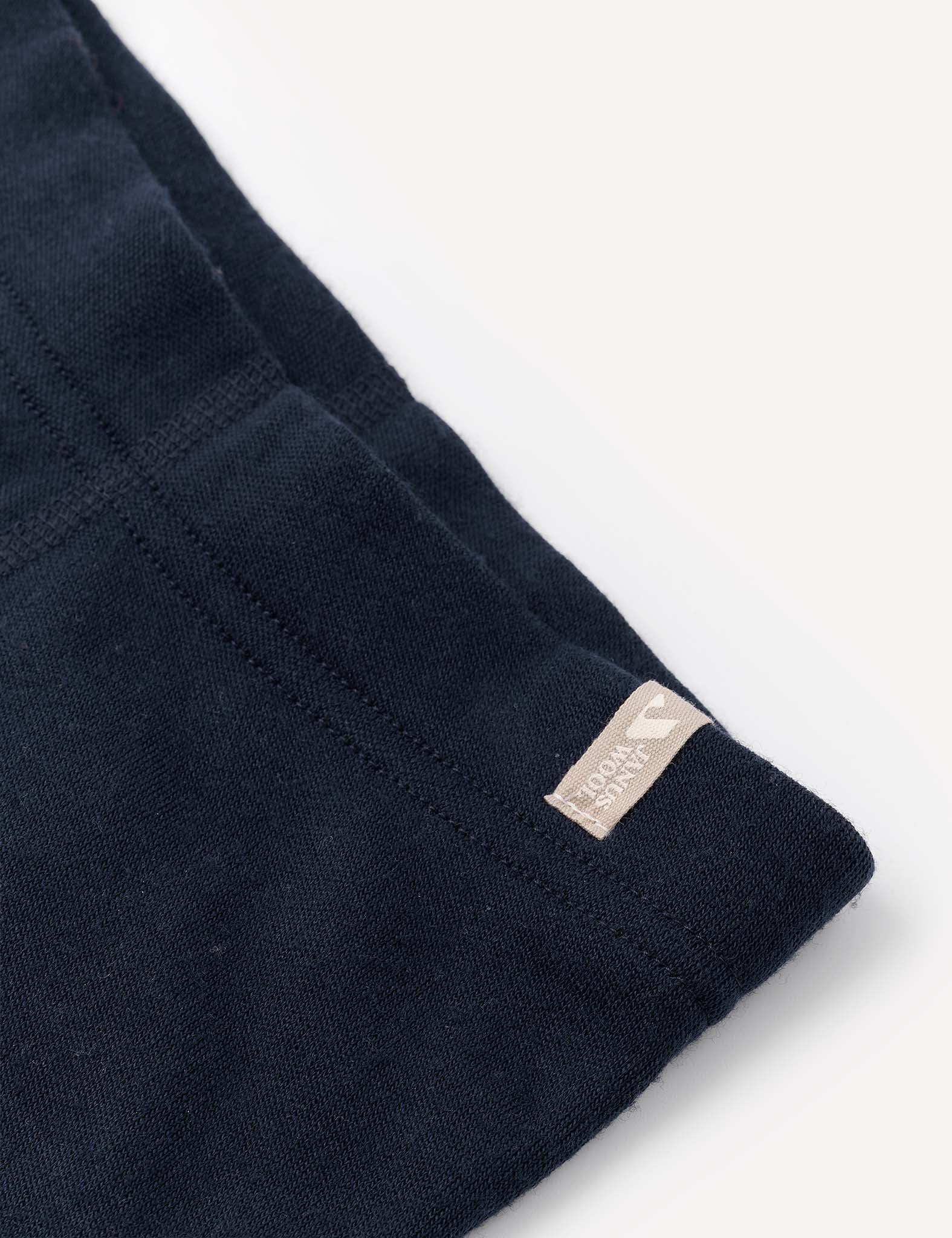 Close-up of a navy blue fabric with visible stitching and a small beige tag that reads KNOWN SUPPLY sewn on the edge, highlighting details characteristic of the Leggings – Merino Baby AirWool.
