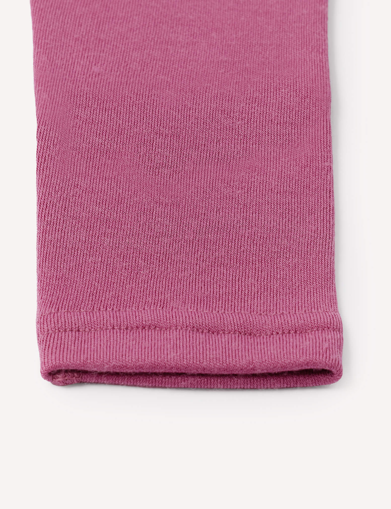 Close-up of the hem of a pink knit fabric sleeve or pant leg, likely from the Leggings – Merino Baby AirWool, highlighting the texture and stitching details against a white background.