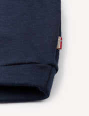 Close-up of a navy blue cuff from the Pullover – Merino Baby AirWool, crafted from soft brushed AirWool fabric, with a small tag featuring a red, white, and blue flag detail stitched into the seam. The background is plain and light-colored.