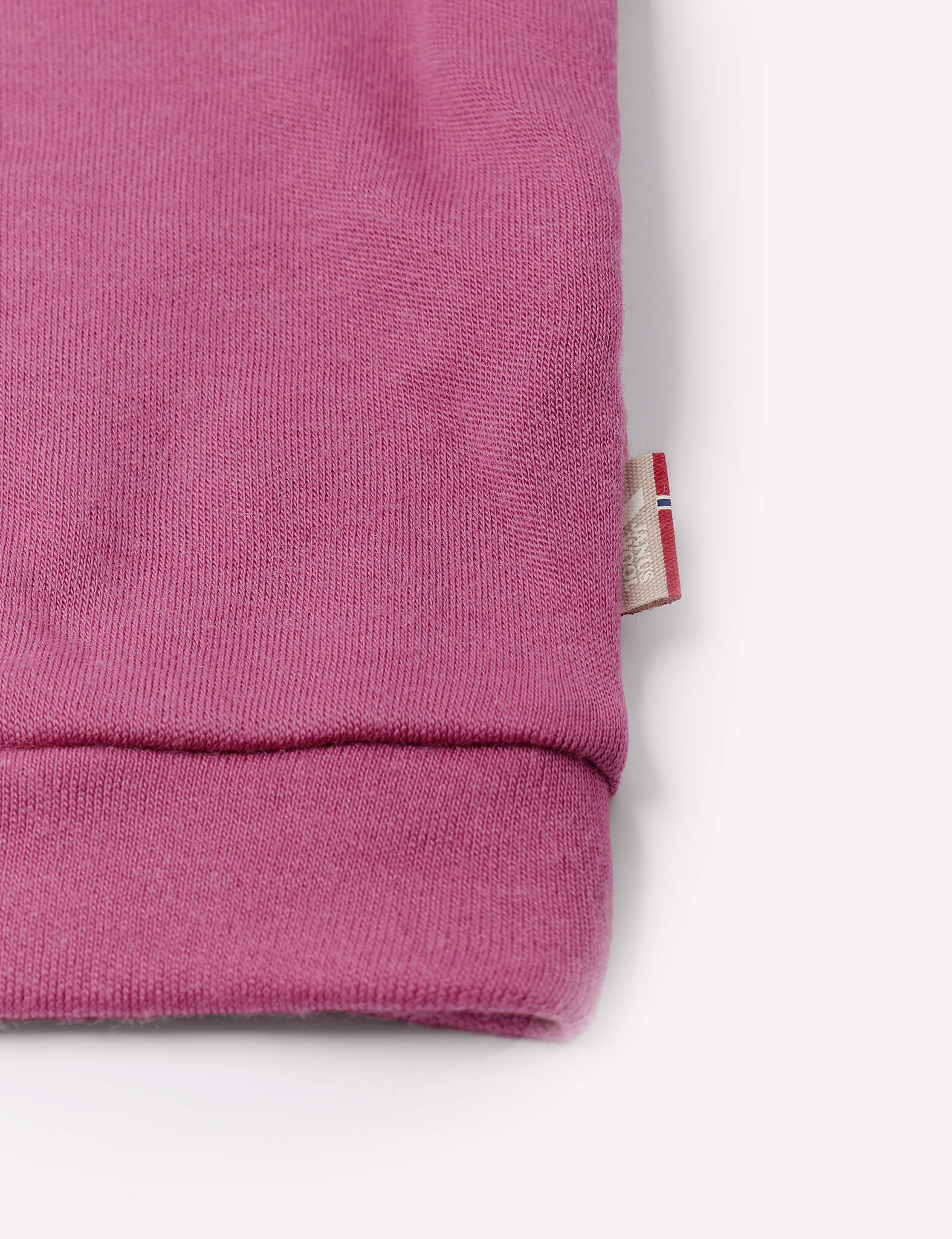 Close-up of a pink sleeve from the Pullover – Merino Baby AirWool, featuring a small tag with a red, white, and blue flag detail on the side. Crafted from breathable insulation, this merino wool jumper is set against a white background.
