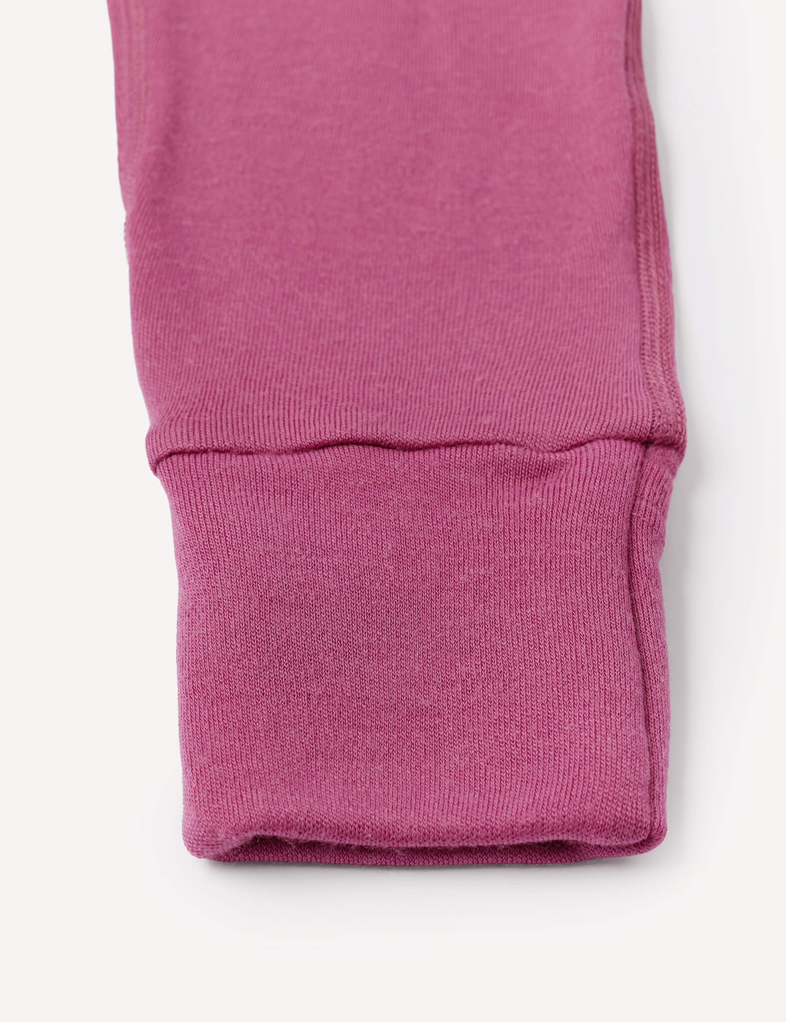 Close-up of a pink ribbed fabric cuff, likely from the sleeve of the Onesie – Merino Baby AirWool, featuring fold-over cuffs and displayed on a white background.