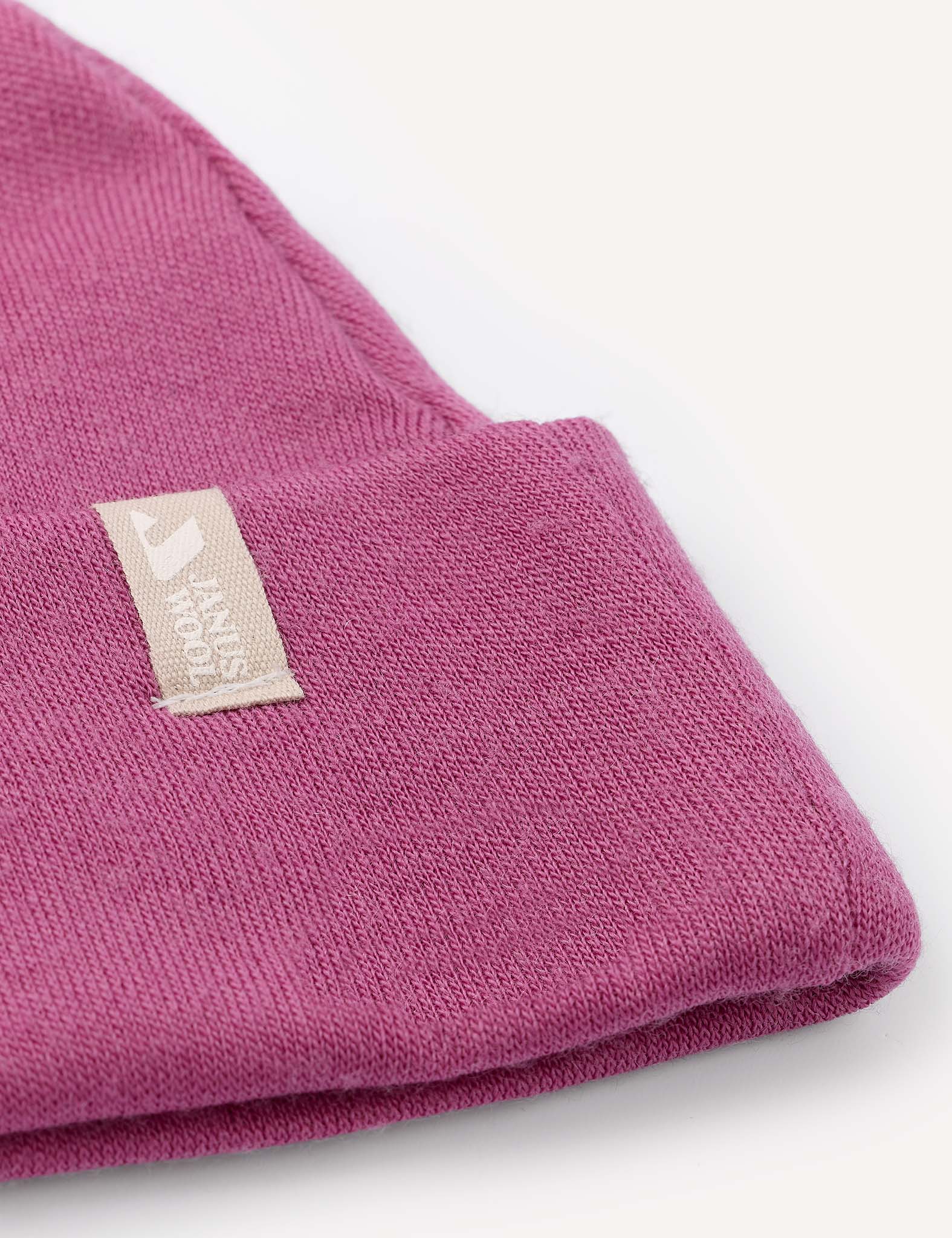 Close-up of a folded pink Beanie – Merino Baby AirWool with a beige fabric tag featuring a white logo and partial text, set against a white background. This warm baby hat provides breathable insulation for comfort.