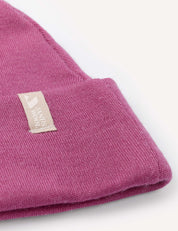 Close-up of a folded pink Beanie – Merino Baby AirWool with a beige fabric tag featuring a white logo and partial text, set against a white background. This warm baby hat provides breathable insulation for comfort.