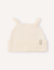 Introducing the Beanie – Merino Baby AirWool in Marshmallow: a soft, cream-colored baby beanie featuring two small, rounded ear-like accents on top and a folded brim. Crafted from breathable merino wool for cozy comfort, it is finished with a small beige tag on the side.