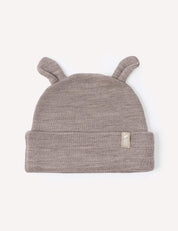 A beige melange merino wool baby beanie, the Beanie – Merino Baby AirWool, features two small ear-like points on top and a folded brim with a small beige fabric tag on the front. This warm hat offers cozy comfort for your little one.