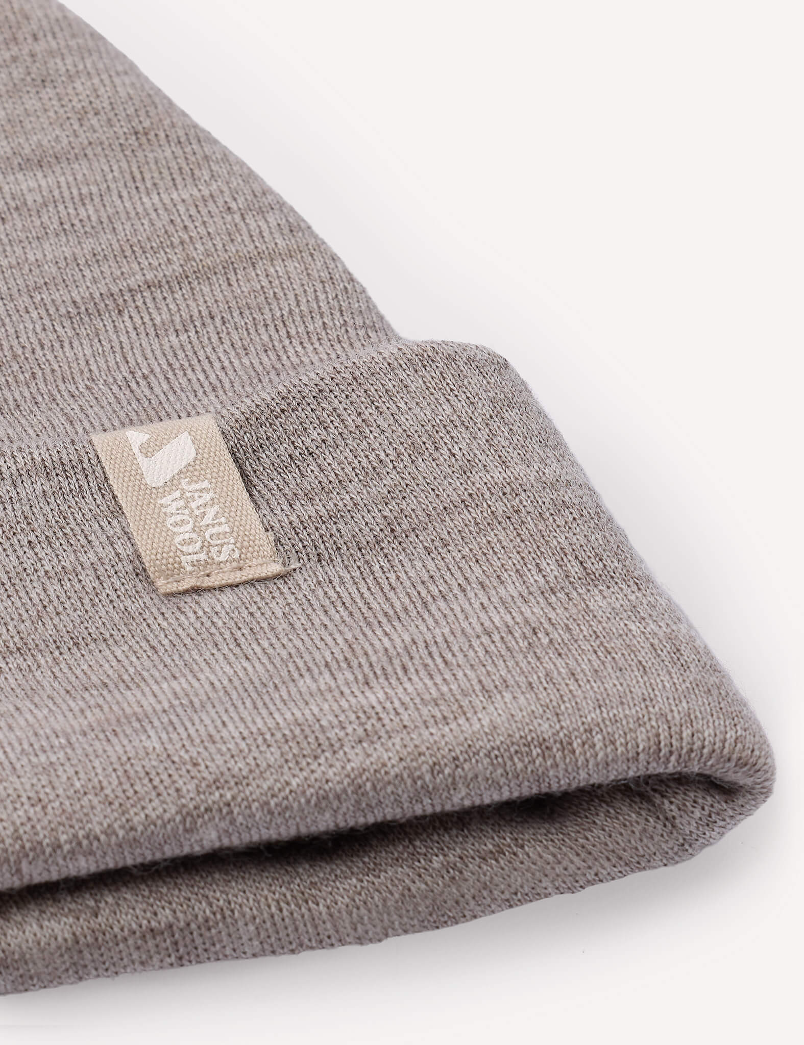 A close-up of a folded, light gray Beanie – Merino Baby AirWool featuring a beige tag that reads KNUS MADE with a small icon beside the text.