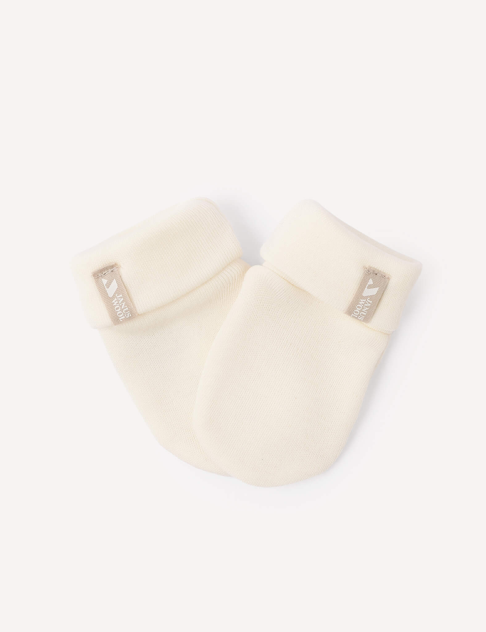 A pair of Mittens – Merino Baby AirWool, crafted from cozy merino wool in a soft cream color, featuring folded cuffs and a small beige tag with white text and a bird logo on each cuff, displayed on a white background.