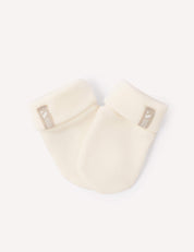 A pair of Mittens – Merino Baby AirWool, crafted from cozy merino wool in a soft cream color, featuring folded cuffs and a small beige tag with white text and a bird logo on each cuff, displayed on a white background.