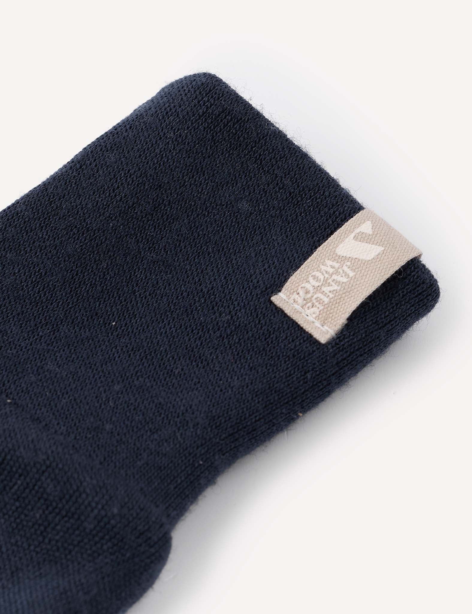 A close-up of a dark navy blue mitten from the Mittens – Merino Baby AirWool collection, featuring a beige fabric tag with small text and a minimal graphic sewn onto the cuff. Crafted from soft merino wool for comfort and warmth.