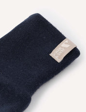 A close-up of a dark navy blue mitten from the Mittens – Merino Baby AirWool collection, featuring a beige fabric tag with small text and a minimal graphic sewn onto the cuff. Crafted from soft merino wool for comfort and warmth.