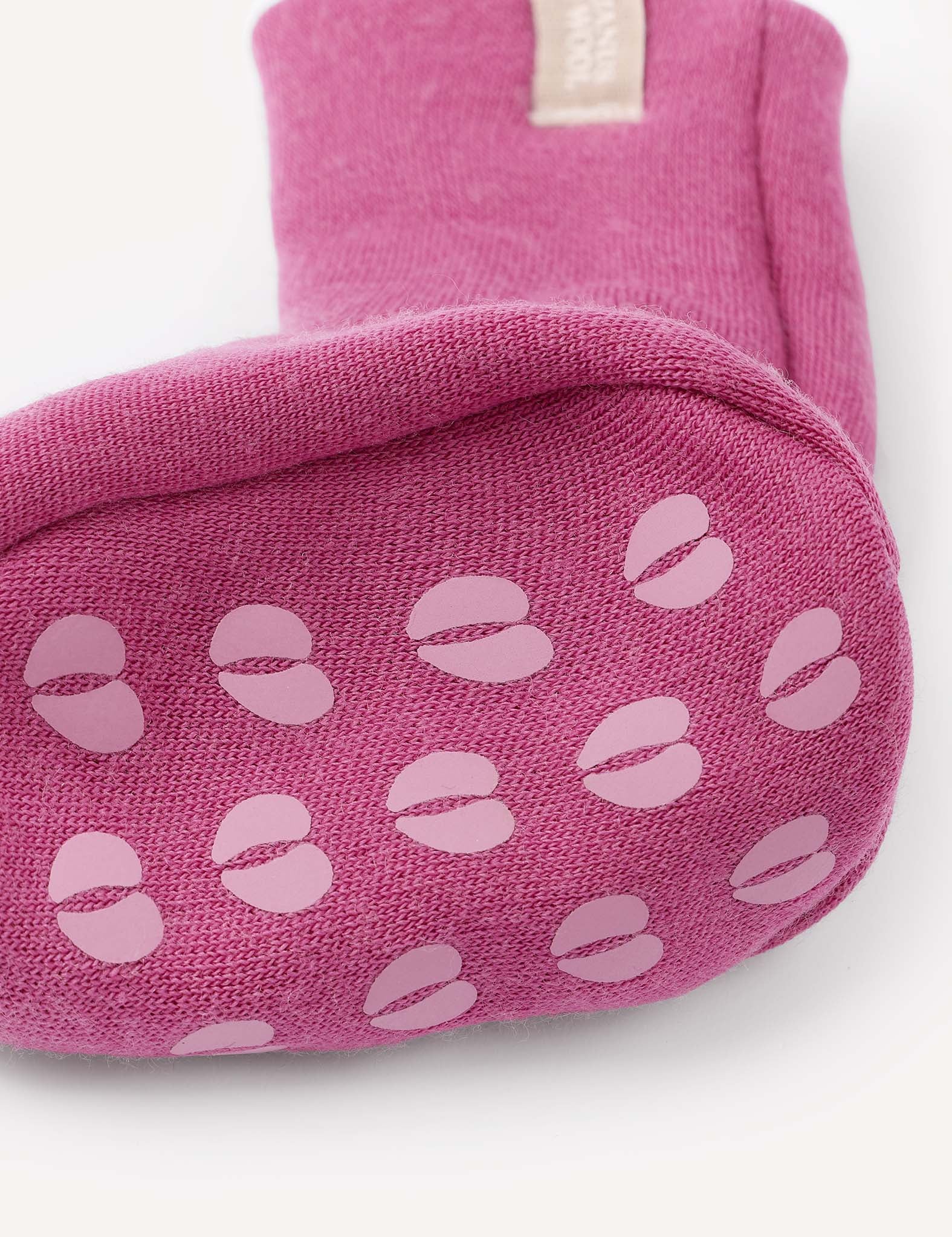 A close-up of the bottom of the Booties – Merino Baby AirWool in pink, featuring light pink non-slip grip patterns shaped like coffee beans or split circles, resembling warm baby booties.