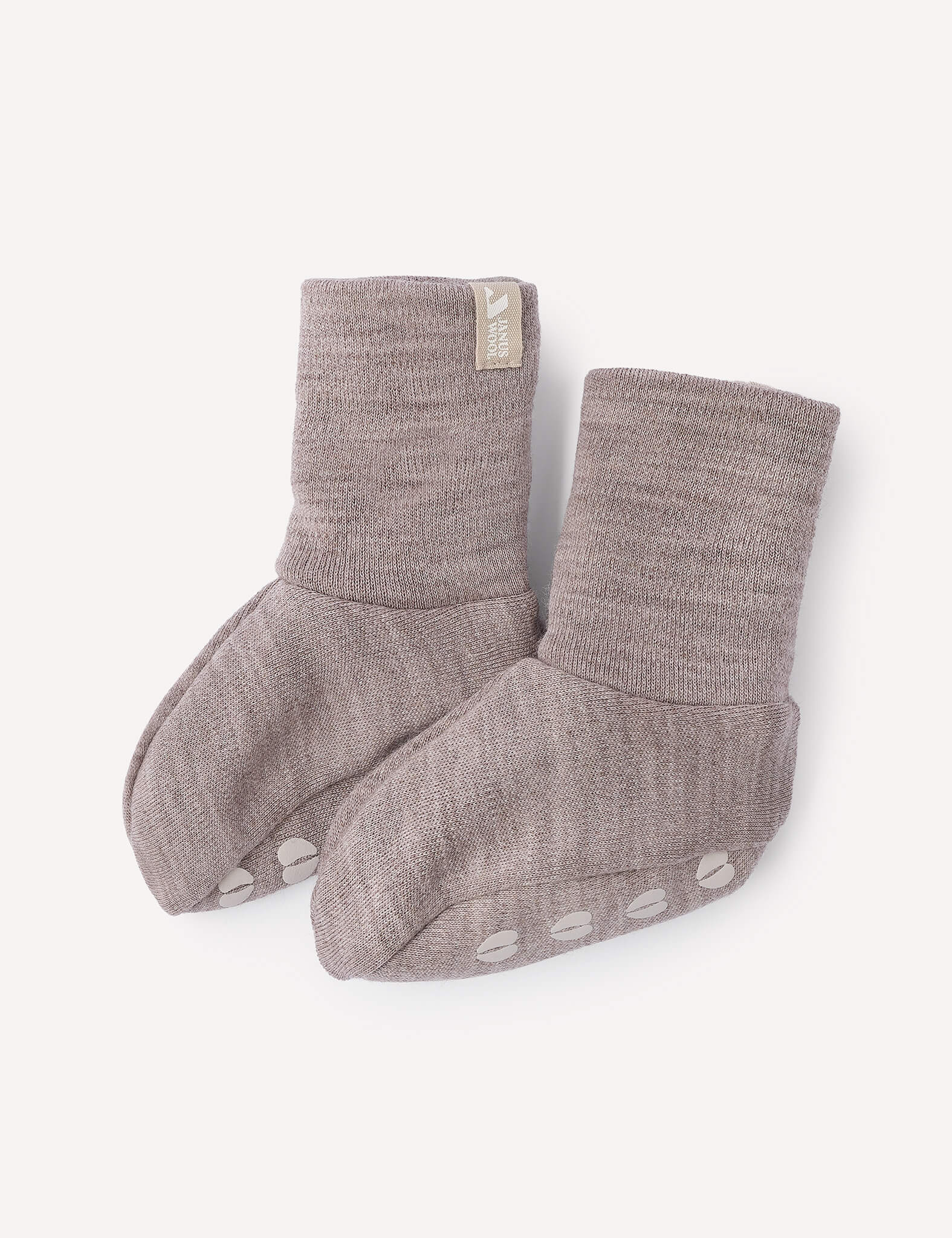 A pair of soft, light brown Booties – Merino Baby AirWool with non-slip white dots on the soles and a small fabric tag on one cuff, displayed on a light background.