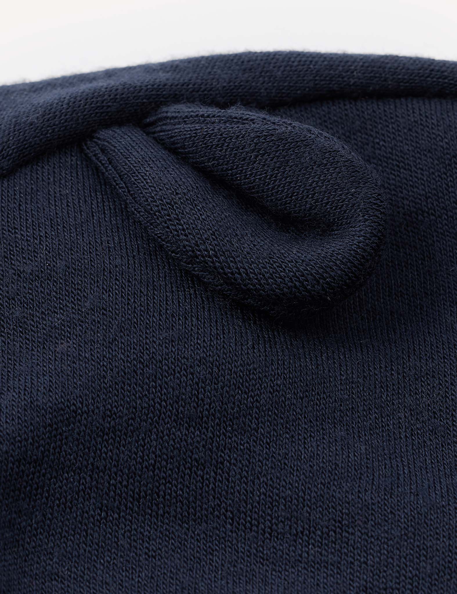 Close-up of the navy blue Merino Baby AirWool Balaclava, showcasing its soft knit fabric with a small, rounded, ear-like detail sewn onto the surface. Crafted from breathable merino wool for gentle comfort.