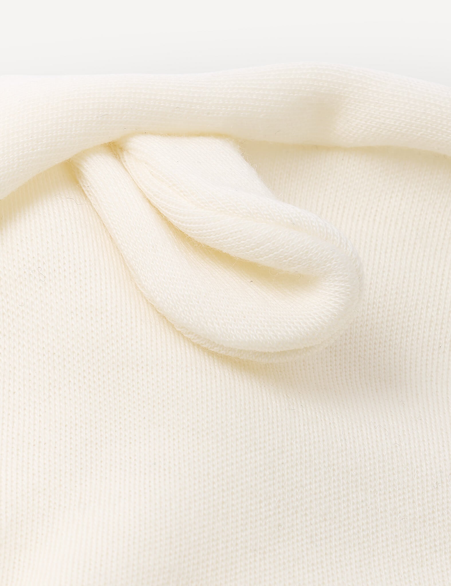 Close-up of a soft, cream-colored knitted fabric with a small, folded loop detail near the top, highlighting the breathable Balaclava – Merino Baby AirWool winter headwear.