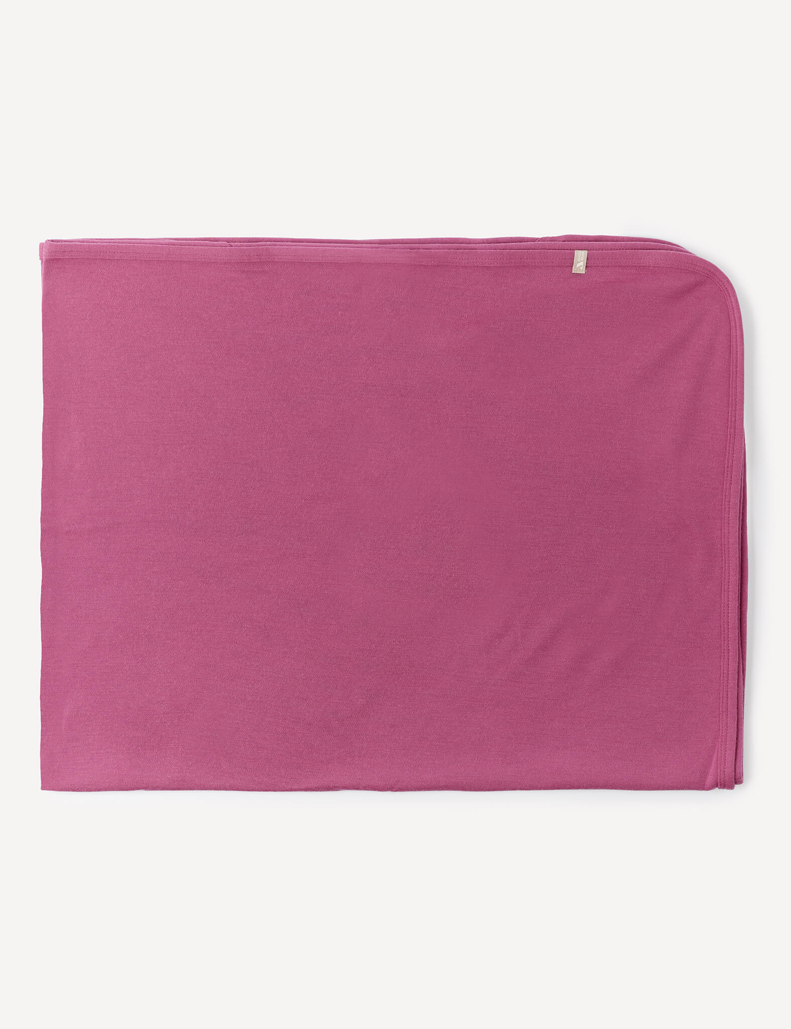 A neatly folded Blanket – Merino Baby AirWool in solid pink, crafted from soft merino wool with a small beige tag in the upper right corner, displayed on a white background.