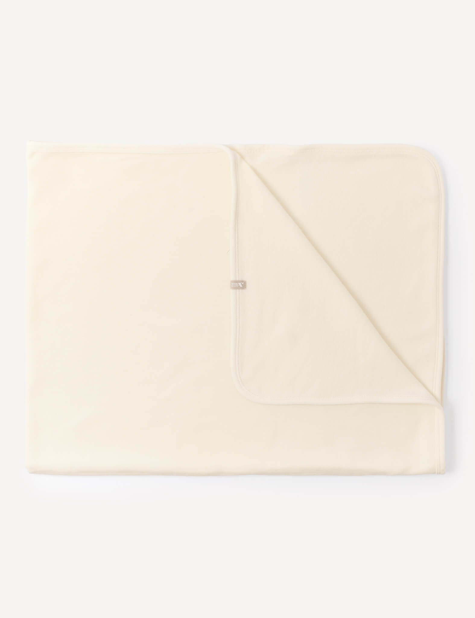 A folded Blanket – Merino Baby AirWool in Marshmallow is laid flat against a white background, with one corner turned over to reveal the underside and a small fabric tag near the edge.