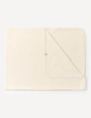 A folded Blanket – Merino Baby AirWool in Marshmallow is laid flat against a white background, with one corner turned over to reveal the underside and a small fabric tag near the edge.