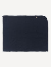 A neatly folded, rectangular Blanket – Merino Baby AirWool in dark navy blue, crafted from soft merino wool with rounded corners on one side, is lying flat against a white background.