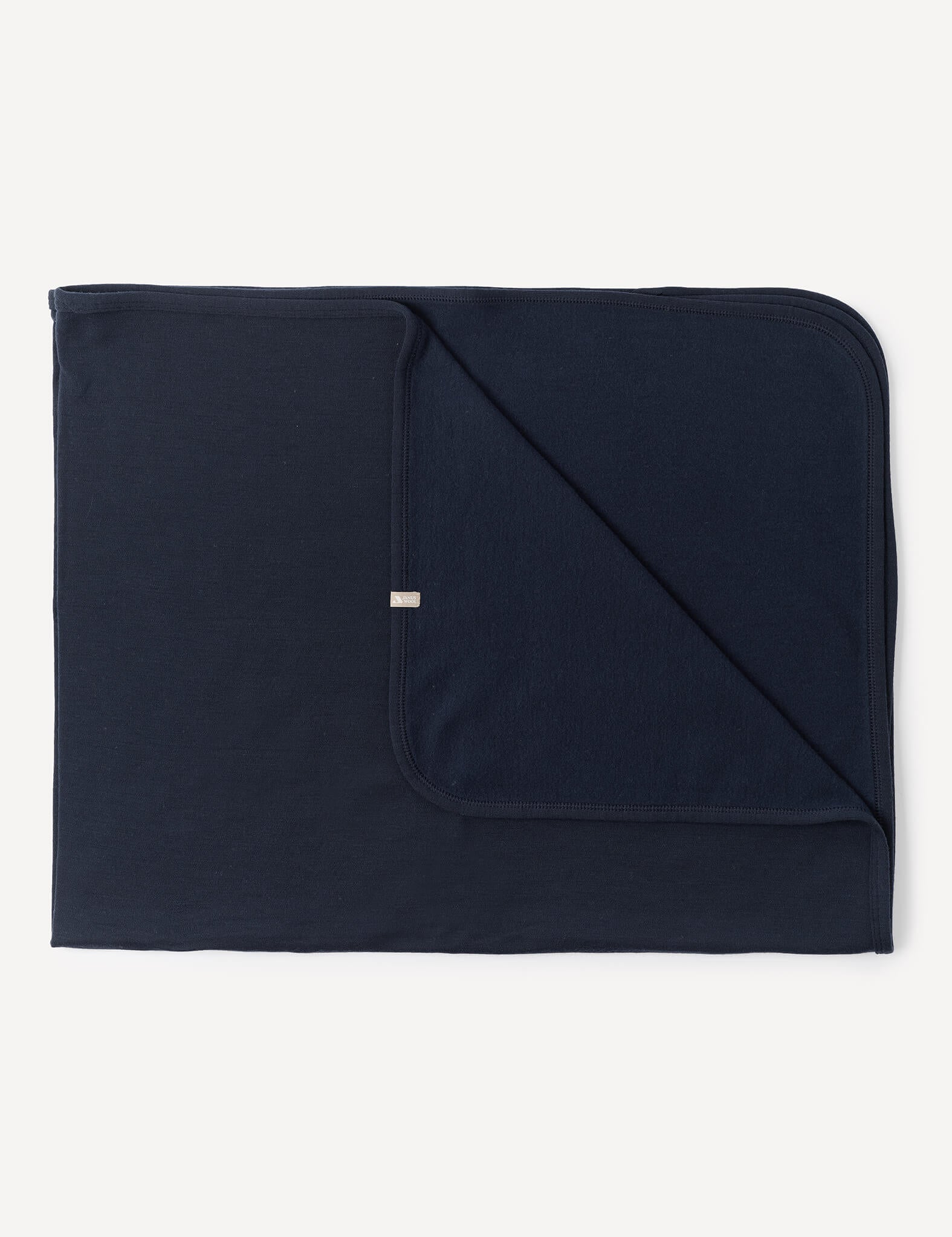 A neatly folded Blanket – Merino Baby AirWool in Navy with one corner flipped to display both sides. The blanket has rounded edges and a small tag on the edge of the folded corner.