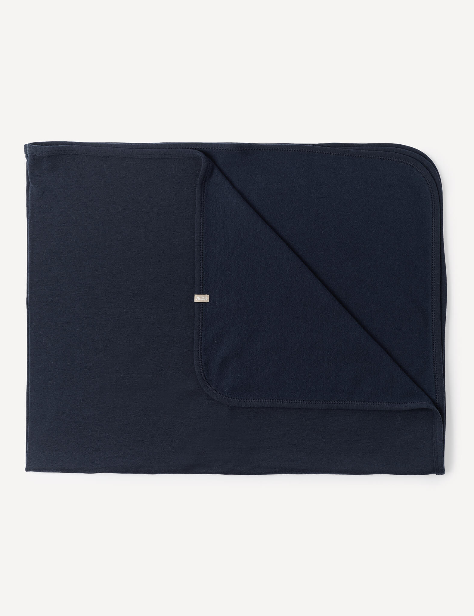 A neatly folded Blanket – Merino Baby AirWool in Navy with one corner flipped to display both sides. The blanket has rounded edges and a small tag on the edge of the folded corner.