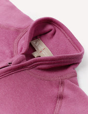Close-up of a folded Jacket – Merino Baby AirWool in mauve or purple, showing the collar, visible stitching, and fabric tag with care instructions. The image highlights the breathable AirWool insulation that ensures comfort.