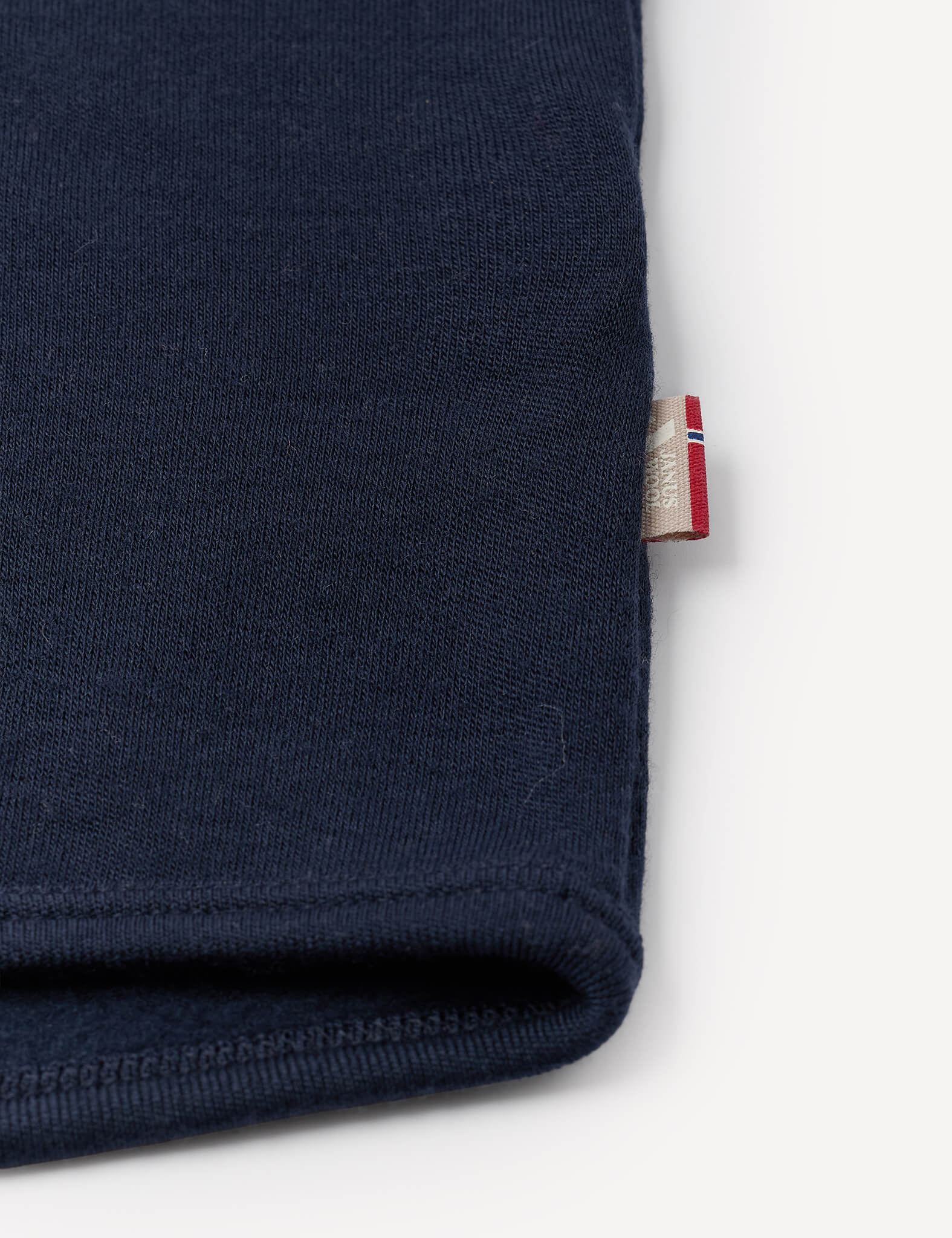 A close-up of the Jacket – Merino Baby AirWool in navy blue, highlighting the sleeve with a small tag displaying a red, white, and blue stripe pattern emerging from the seam, set against a white background.