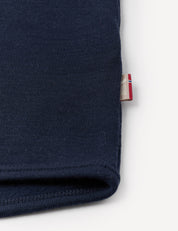 A close-up of the Jacket – Merino Baby AirWool in navy blue, highlighting the sleeve with a small tag displaying a red, white, and blue stripe pattern emerging from the seam, set against a white background.