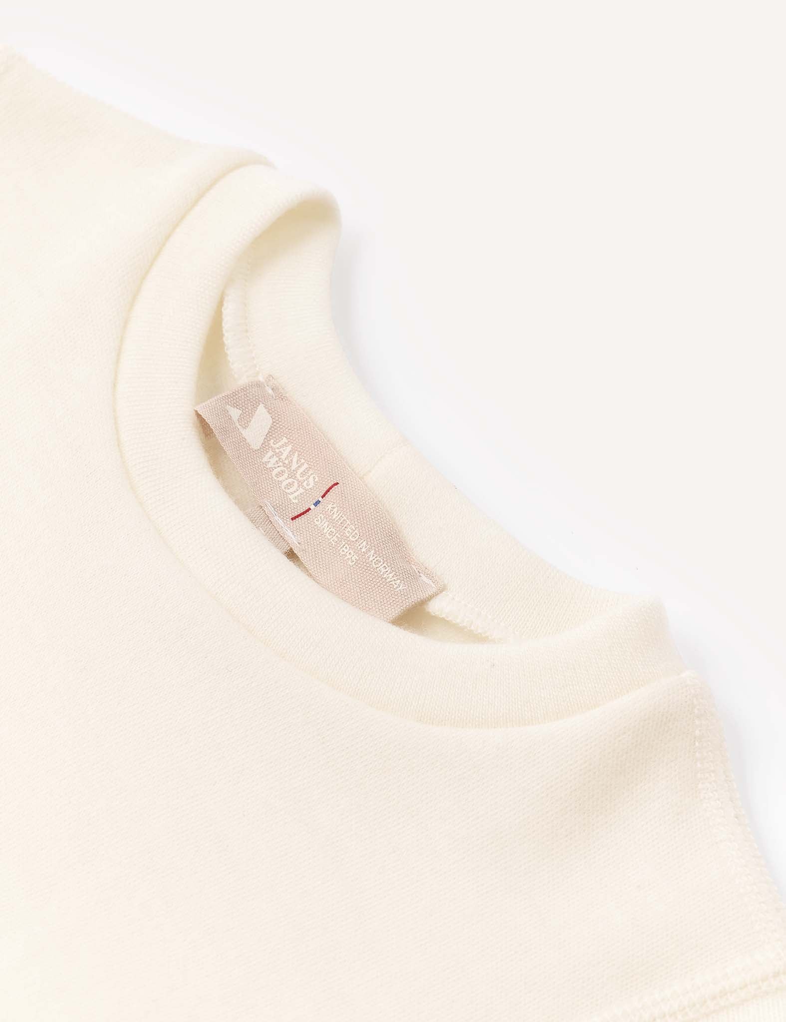 Close-up of the collar and tag of an off-white, long-sleeve Body – Merino Baby AirWool shirt, featuring a beige woven label with text. The soft, slightly textured fabric emphasizes its breathable comfort.