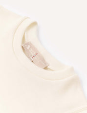 Close-up of the collar and tag of an off-white, long-sleeve Body – Merino Baby AirWool shirt, featuring a beige woven label with text. The soft, slightly textured fabric emphasizes its breathable comfort.