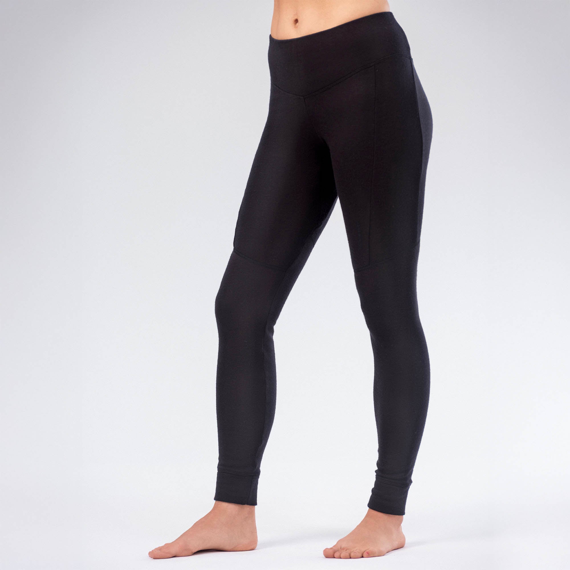 A person stands barefoot on a light background, wearing AirWool 260 Women Merino leggings. The high-waisted, fitted black leggings are ankle-length, breathable, warm, and have a smooth design with no visible logos. Upper body not shown.