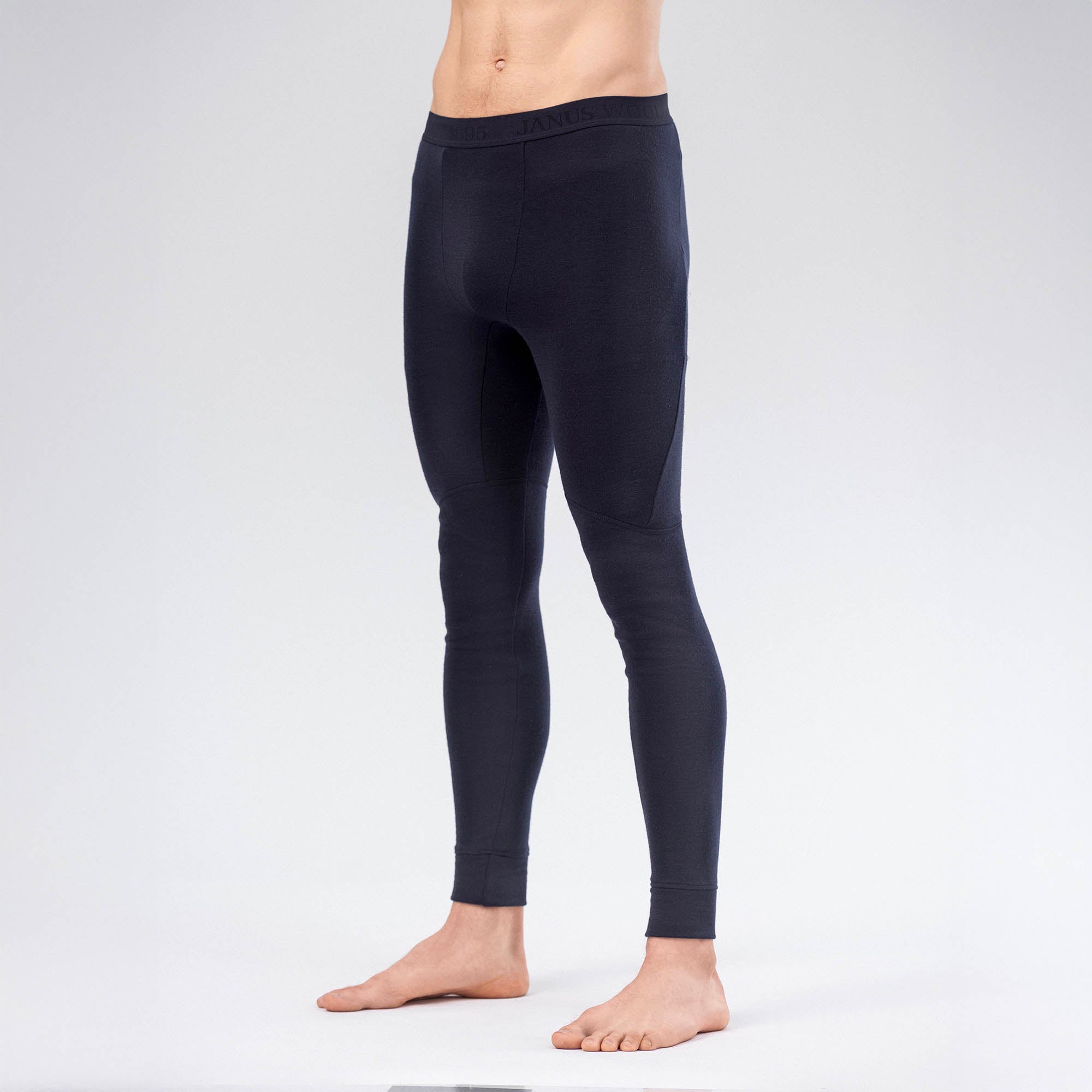 A barefoot person wears fitted, dark-colored Leggings Merino – AirWool 260 Men against a light gray background, showcasing the fabric’s warmth and breathability. Only the legs are visible; the upper body is out of frame.
