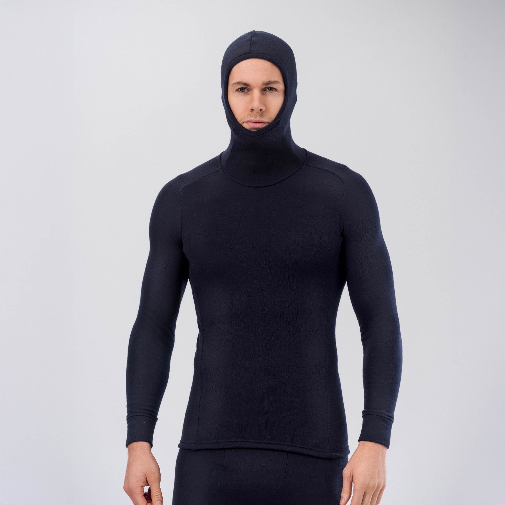 A person wearing the Hooded Jersey Merino – AirWool 260 Men, a fitted black merino wool hoodie with long sleeves that covers the head and neck, stands against a plain light background. The breathable fabric ensures comfort.