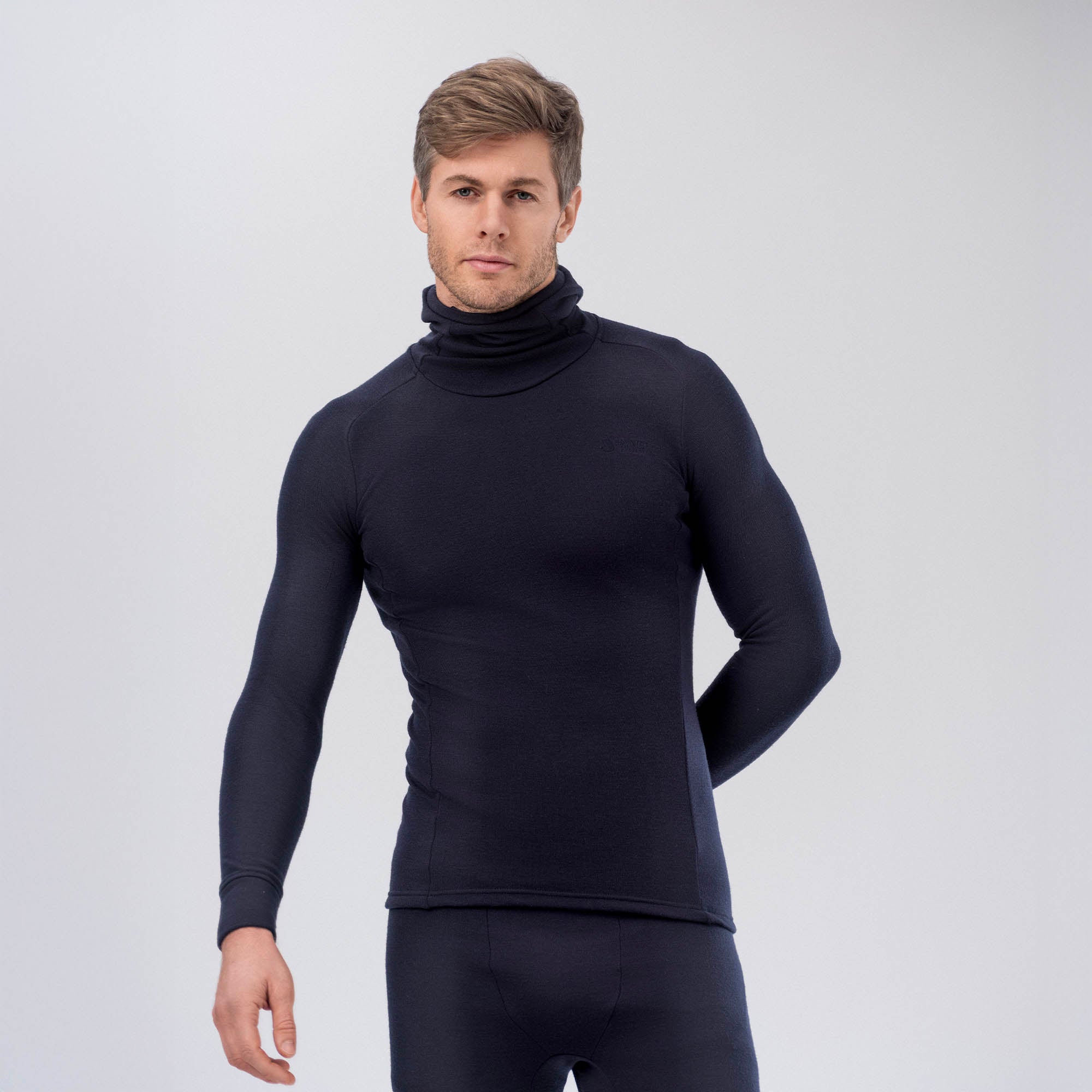 A man stands against a plain light background, facing forward with one hand behind his back, wearing the AirWool 260 Men Hooded Jersey Merino in black as a matching long-sleeve top and bottoms.