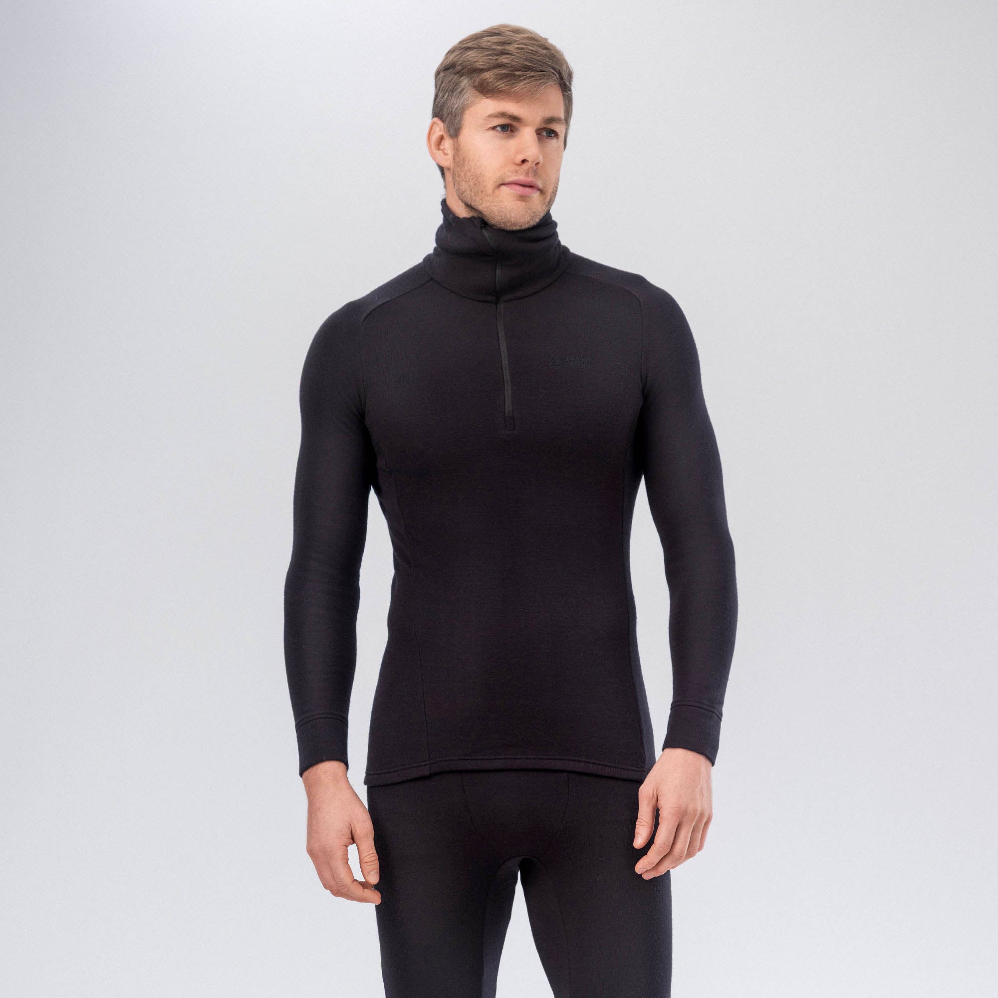 A man wearing the black Polo Zip Merino – AirWool 260 Men stands against a plain light gray background, paired with matching black bottoms.
