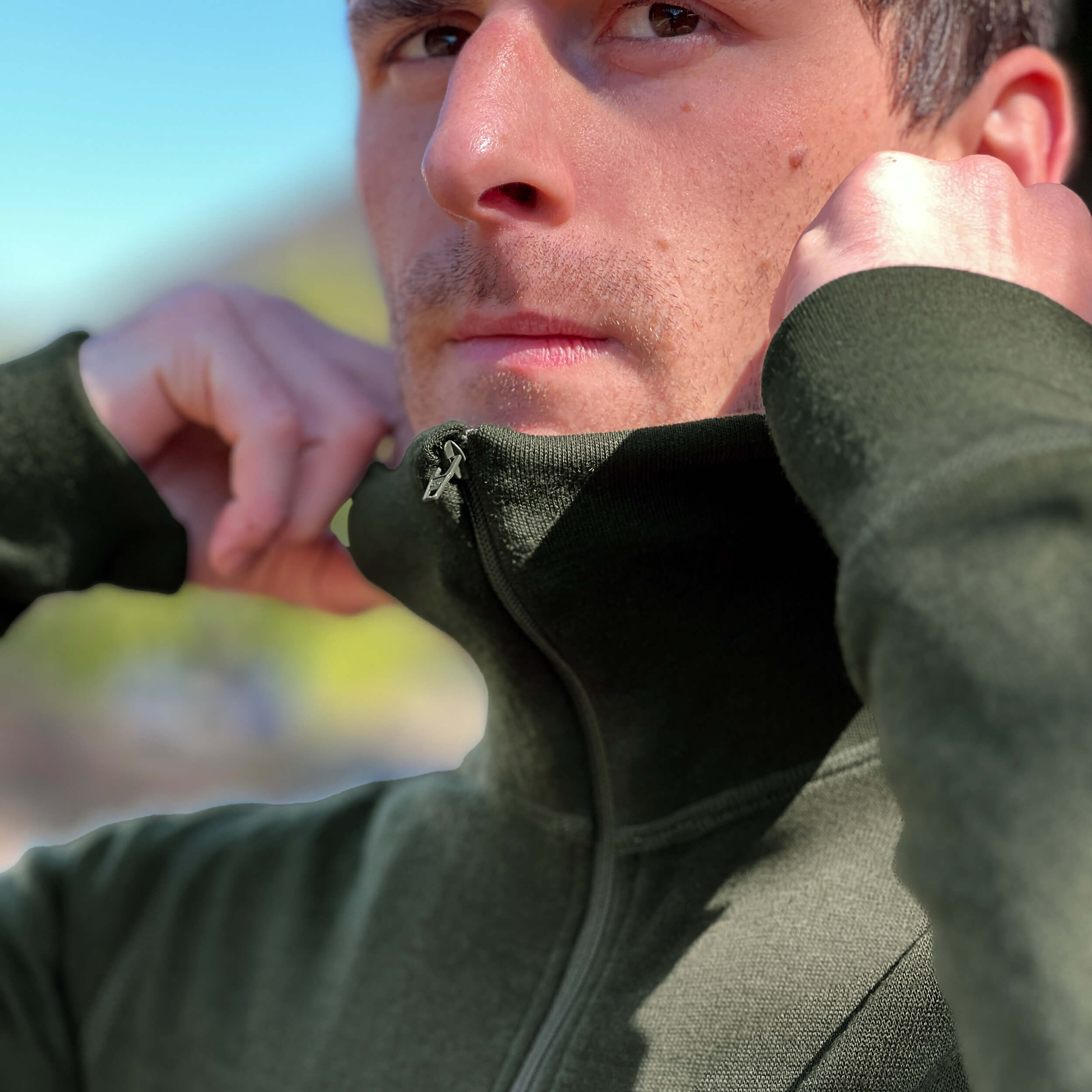 Man wearing a Janus Norse Merino Polo in green, with a blurred natural background
