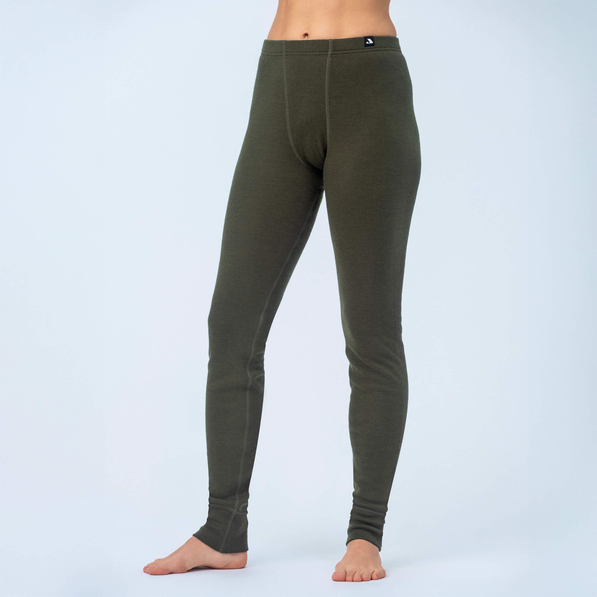 A barefoot individual stands on a light surface against a plain background, wearing olive green Double Layer Leggings - Norse Merino Unisex. The image is cropped above the waist, focusing on the lower torso and legs.