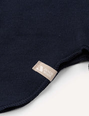 Close-up of a dark blue knitted fabric with a beige label sewn onto the edge, set against a white background. The texture highlights the premium quality of the Merino Kids AirWool balaclava, designed to keep children warm on chilly days.