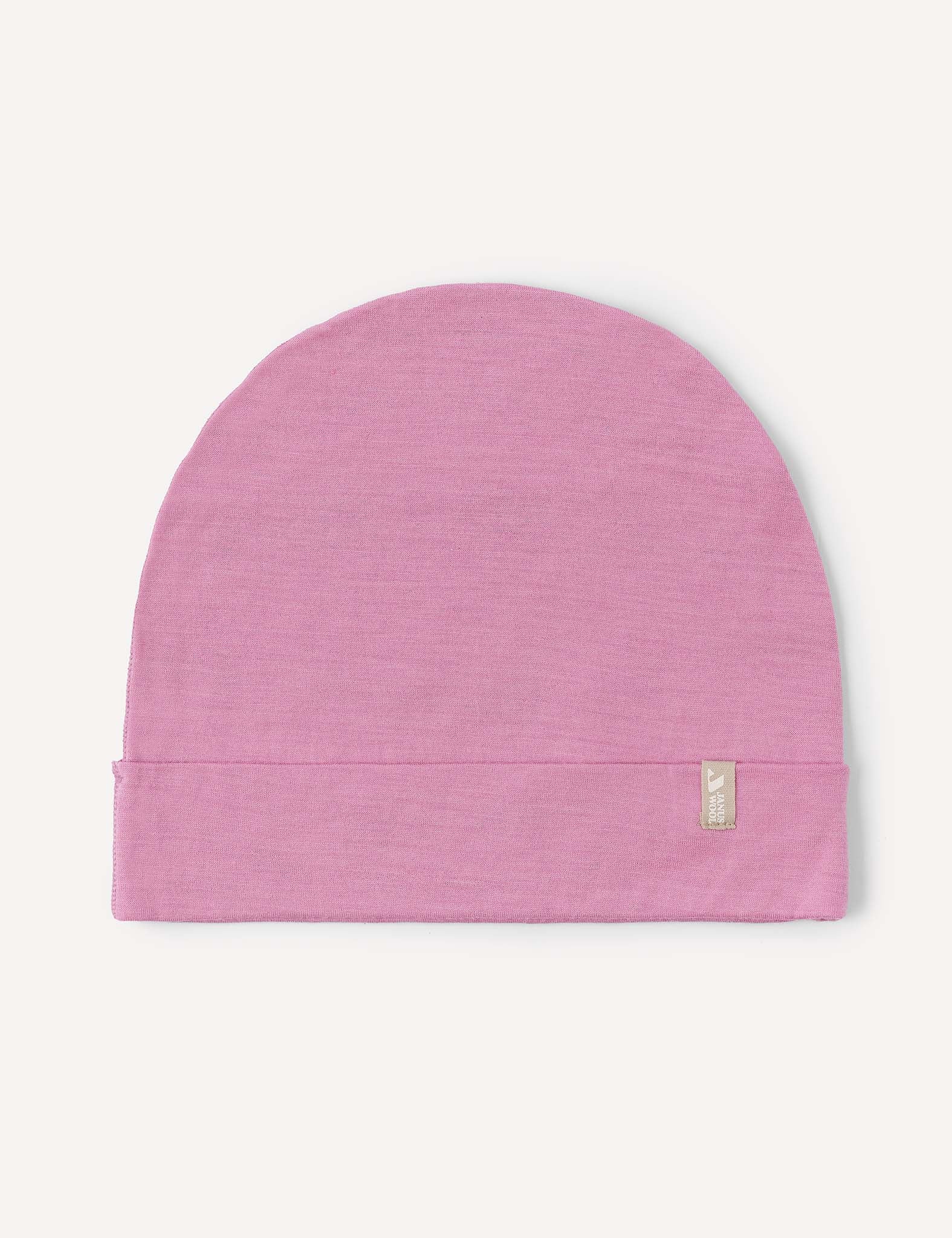 A Beanie – Merino Kids Light in the color Mauve Orchid is laid flat on a white background, featuring a small beige tag with subtle writing attached to its folded edge.