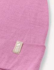 Close-up of the Beanie – Merino Kids Light in pink, featuring a beige tag sewn onto the edge with a logo and text.