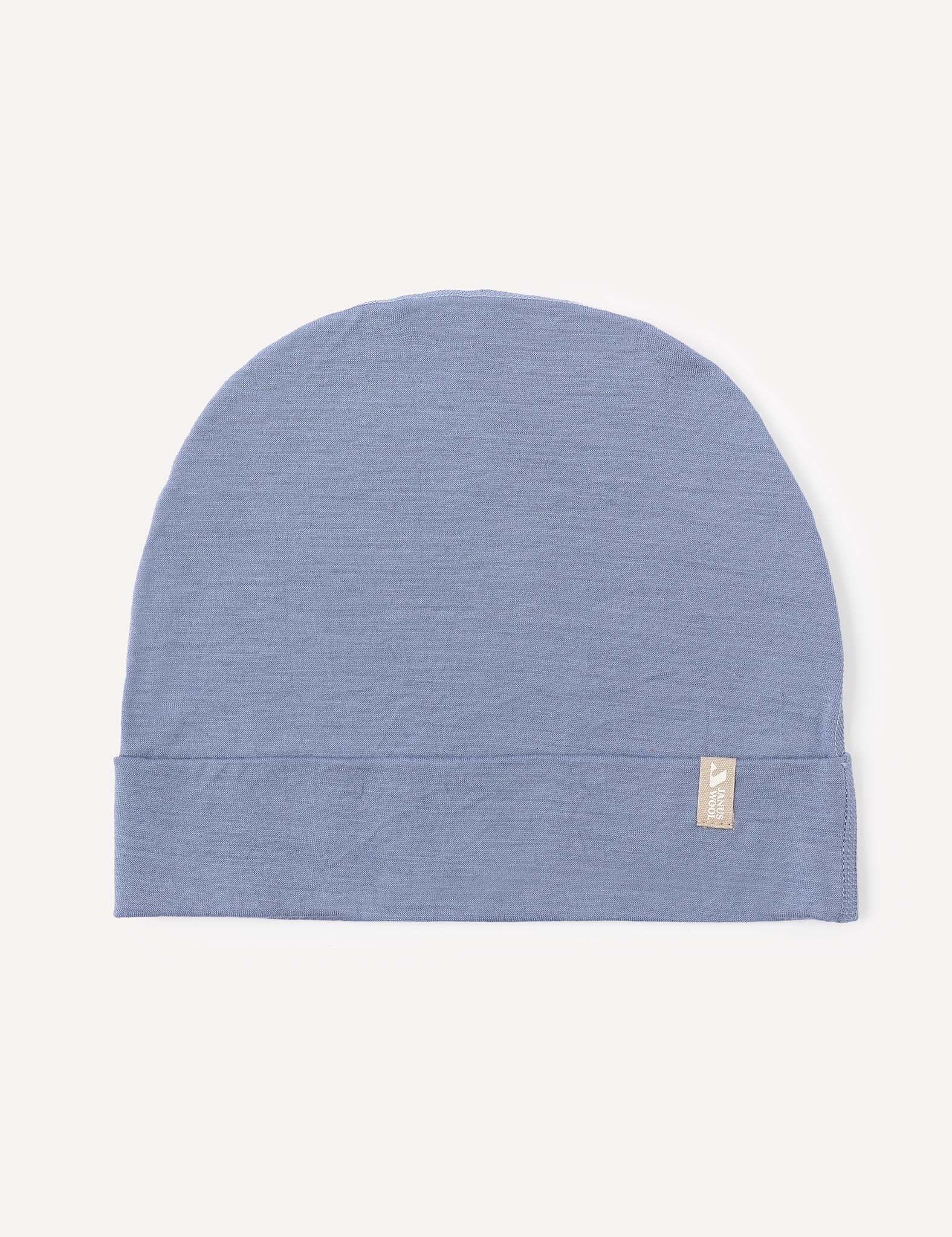A soft merino wool beanie in the color Troposphere, featuring a small beige tag on the cuff, is displayed flat on a plain white background.