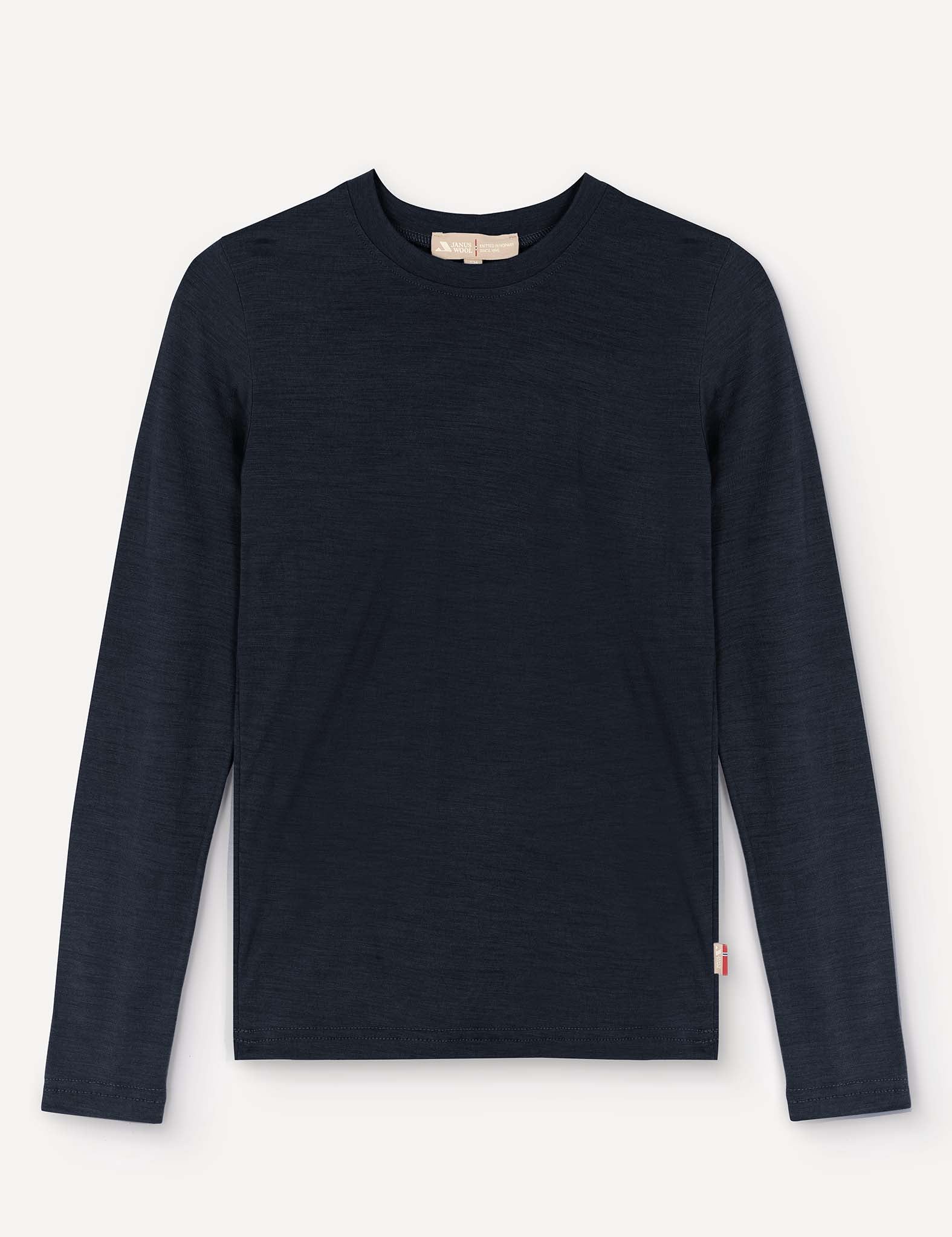 A navy “Crewneck – Merino Kids Light” long-sleeved shirt made from soft merino wool is laid flat on a light background. It features a small white and red tag on the lower left side near the hem.