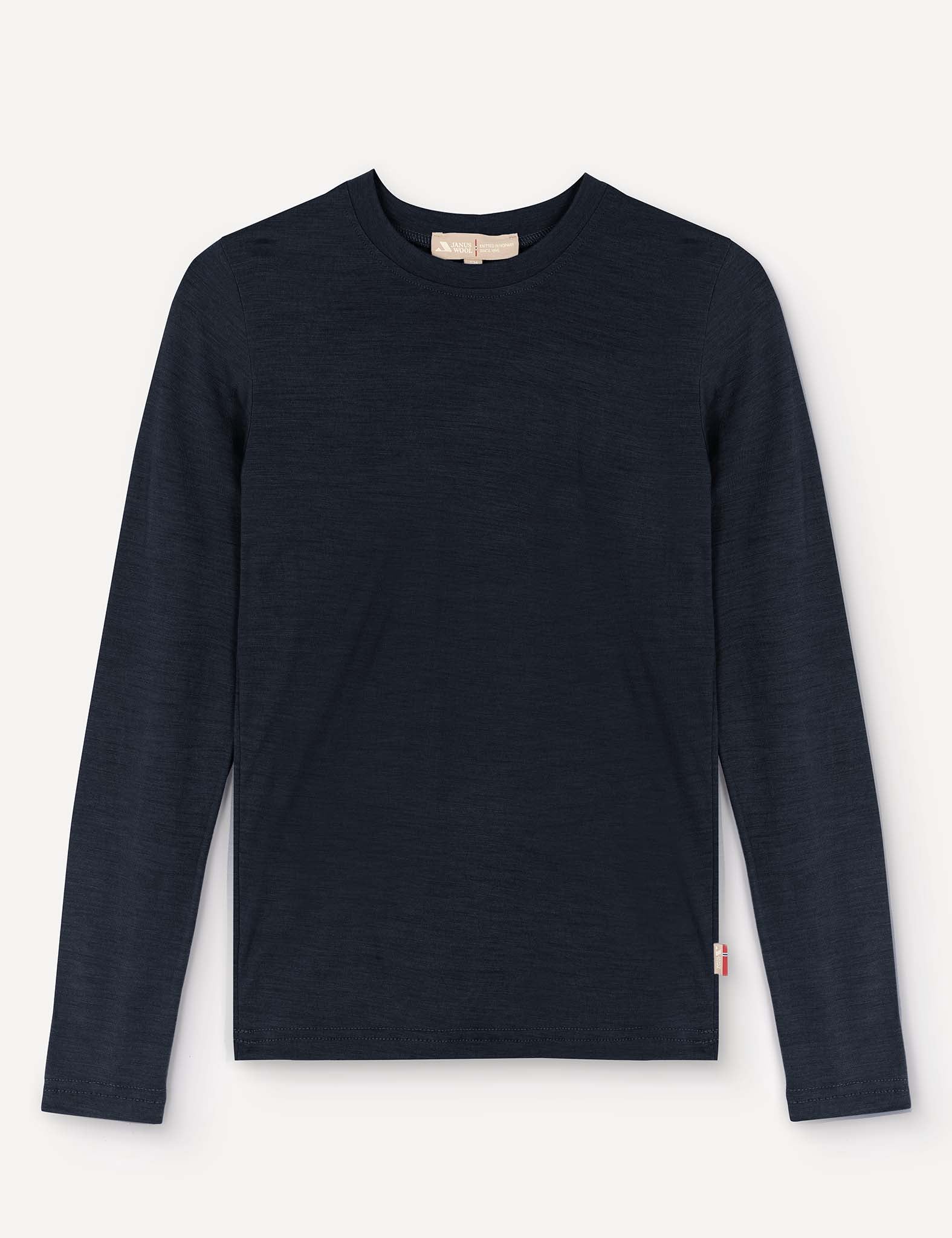 A navy “Crewneck – Merino Kids Light” long-sleeved shirt made from soft merino wool is laid flat on a light background. It features a small white and red tag on the lower left side near the hem.