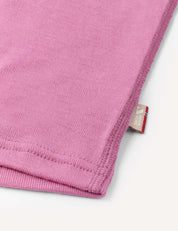 Close-up of the hem of the pink Crewneck – Merino Kids Classic Rib, revealing fine ribbed wool jersey fabric, detailed stitching, and a small beige tag with text and a logo.