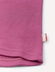 Close-up of the corner of the Crewneck – Merino Kids AirWool in pink, showing visible stitching and a small beige tag with a red and blue stripe along the right edge.