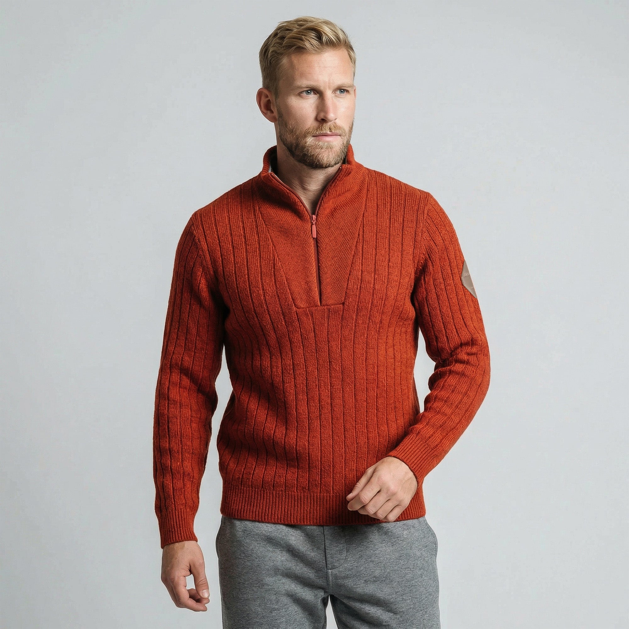 A man with blonde hair and a beard wears the Finse sweater - Rust and gray sweatpants, standing against a plain light gray background.
