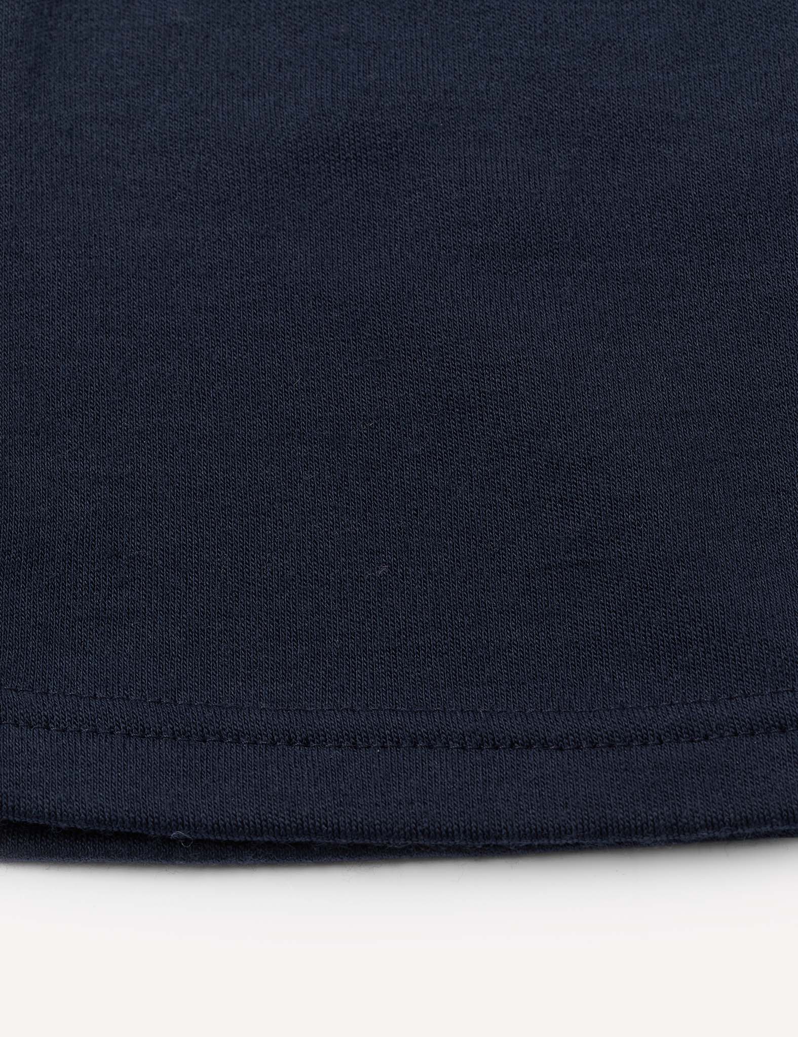 Close-up of the hem of the Flarepants – Merino Kids AirWool in dark navy blue, highlighting the merino wool fabric and detailed stitching near the bottom edge against a light background.