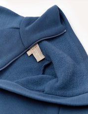 A close-up of the Merino Kids AirWool Jacket in blue displays its soft inner fleece lining—reminiscent of premium wool garments—and a beige clothing tag with red and black text, partially tucked inside.
