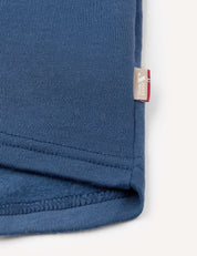 Close-up of the hem of the Jacket – Merino Kids AirWool in blue, featuring a small beige tag with text and a red, white, and blue accent on the edge, set against a plain background.