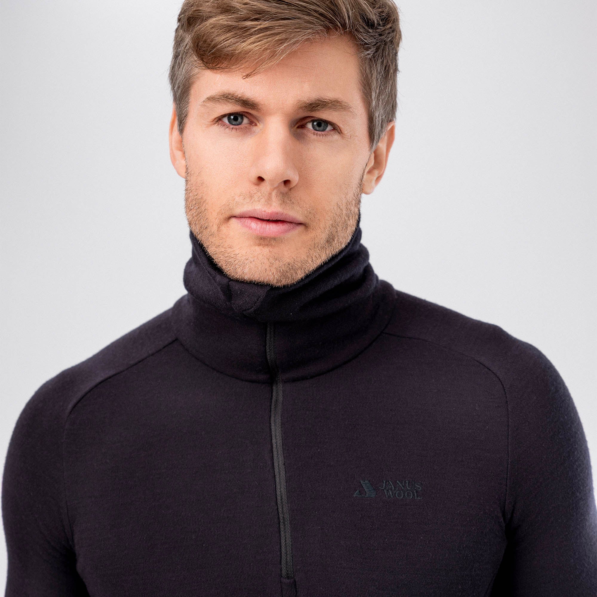 A man with light brown hair and blue eyes wears the Polo Zip Merino – AirWool 260 Men, standing calmly against a plain light background and looking directly at the camera.